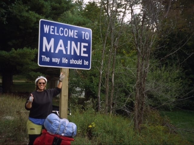 Liza McQuade next to a "Welcome to Maine" road sign